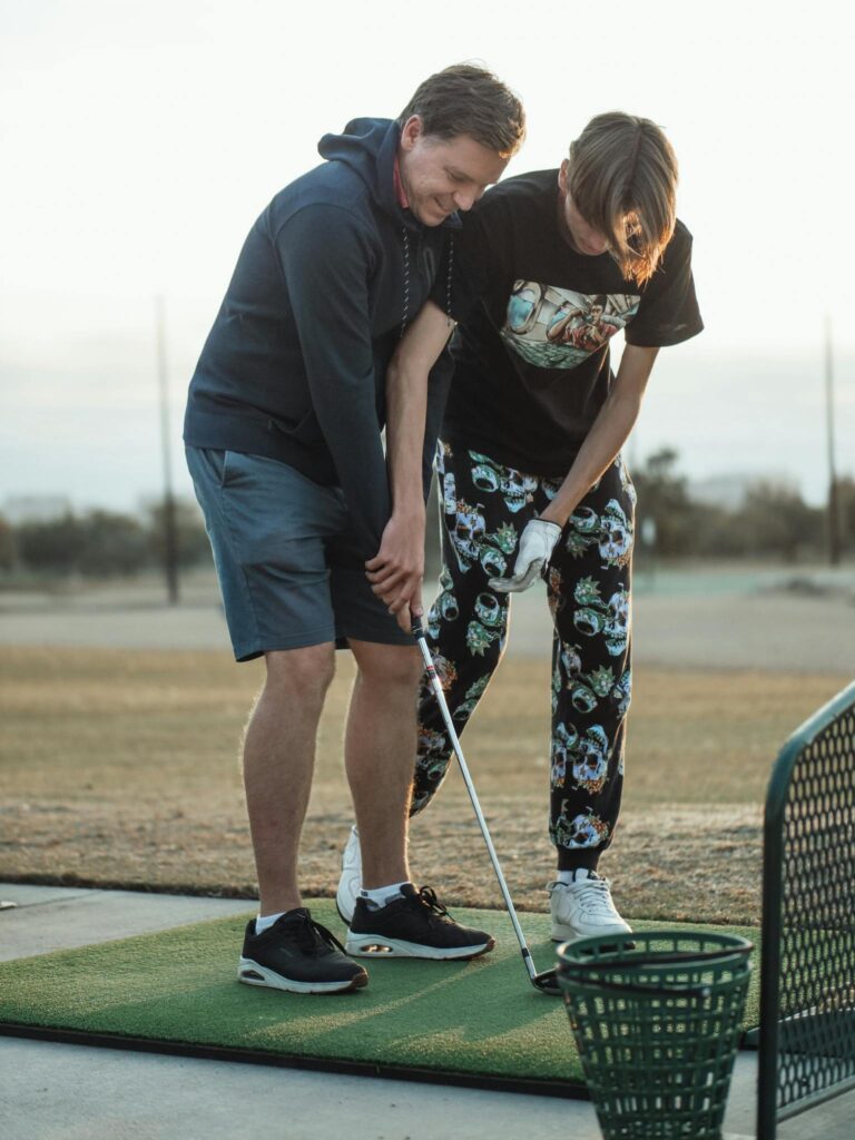 A father and teenage son bonding while practicing golf together outdoors.
