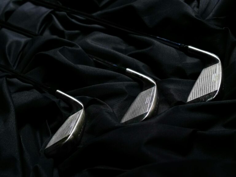 Elegant close-up of metal golf clubs placed on creased black fabric, ideal for sports equipment themes.