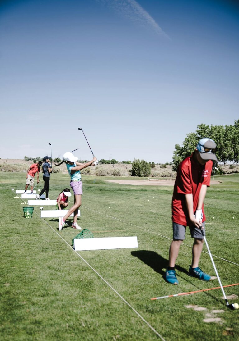 Teen golfers practicing their swings at a driving range on a sunny day.